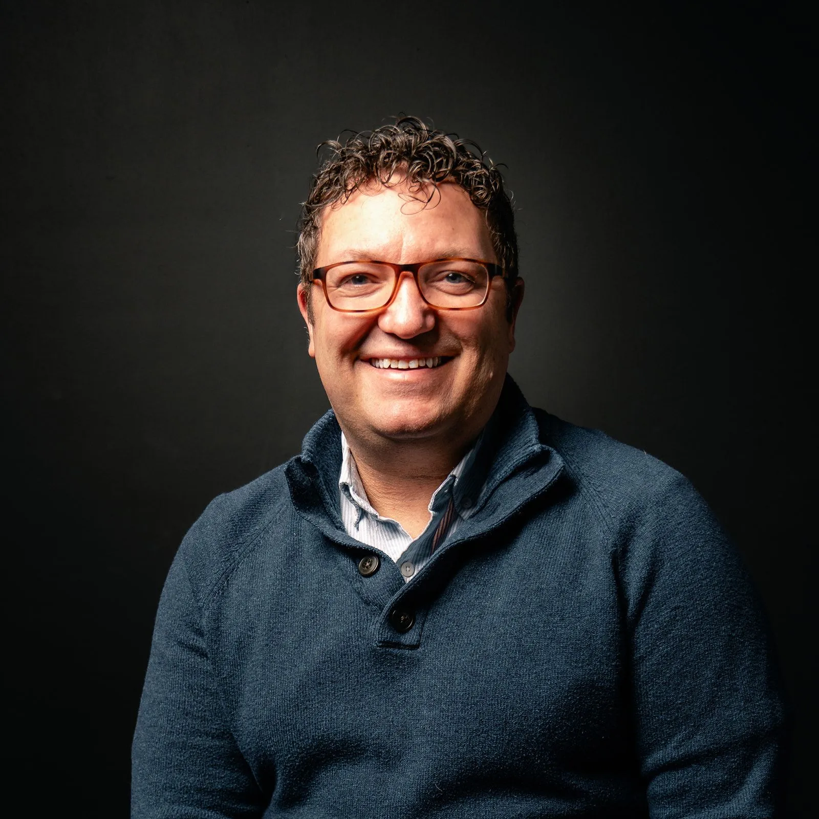 Billy Mawhiney smiling in a head-and-shoulders portrait against a dark background